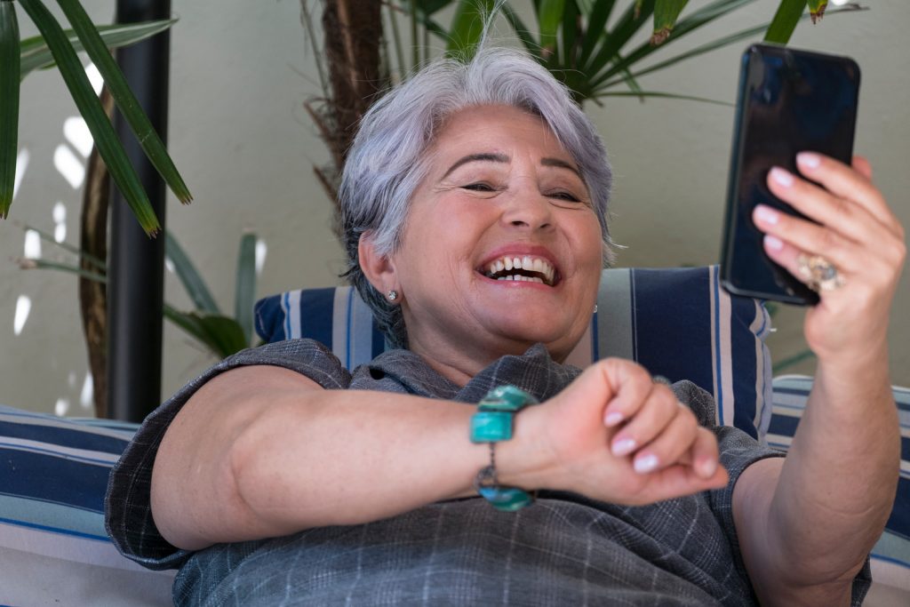 Elderly woman using a phone and smiling - benefits of technology for seniors I StrongLink Technology
