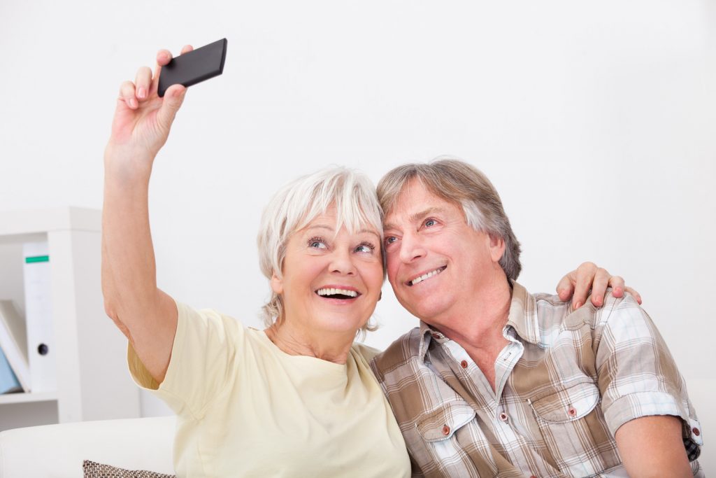 Senior Woman Using Mobile Phone Photographing Self With Husband - Communication Apps for Seniors I StrongLink Technology