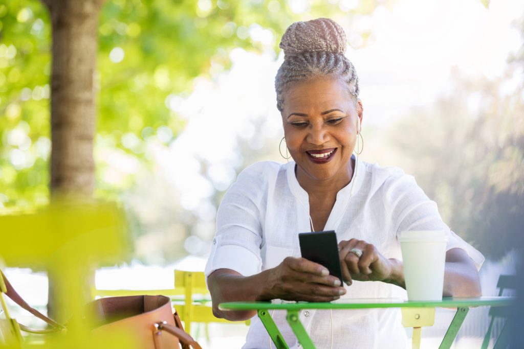 While outdoors in a park, a beautiful senior woman uses her mobile app on her smartphone to look at social media I StrongLink Technology