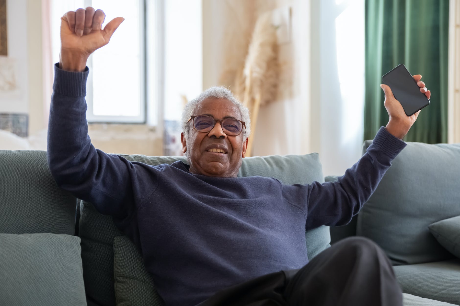 elderly man sitting on sofa while holding a cellphone I How Seniors Can Overcome Lack of Familiarity with Technology I StrongLink Technology I Sharanda Strong Henry