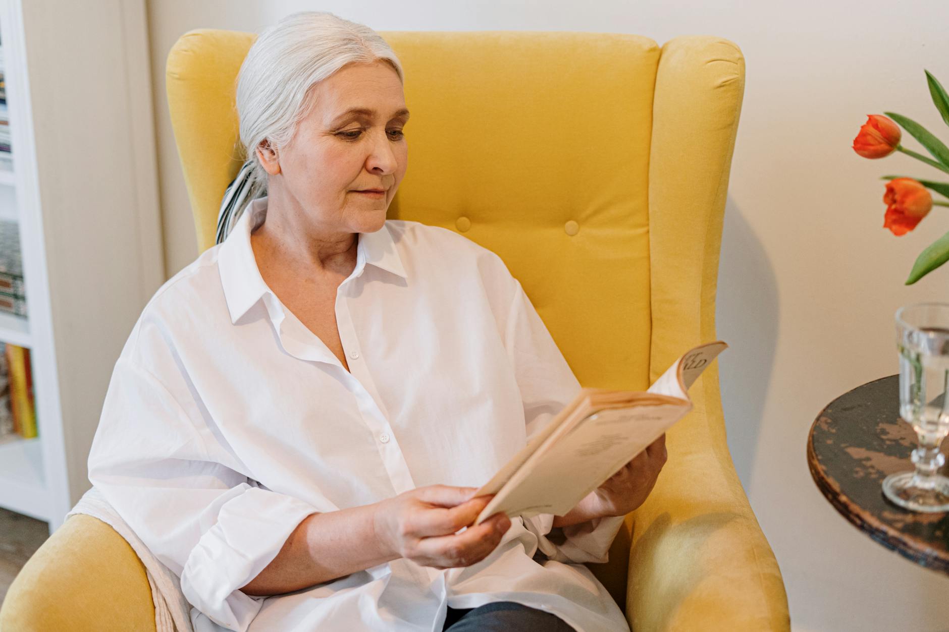 an elderly woman sitting on a couch reading a book