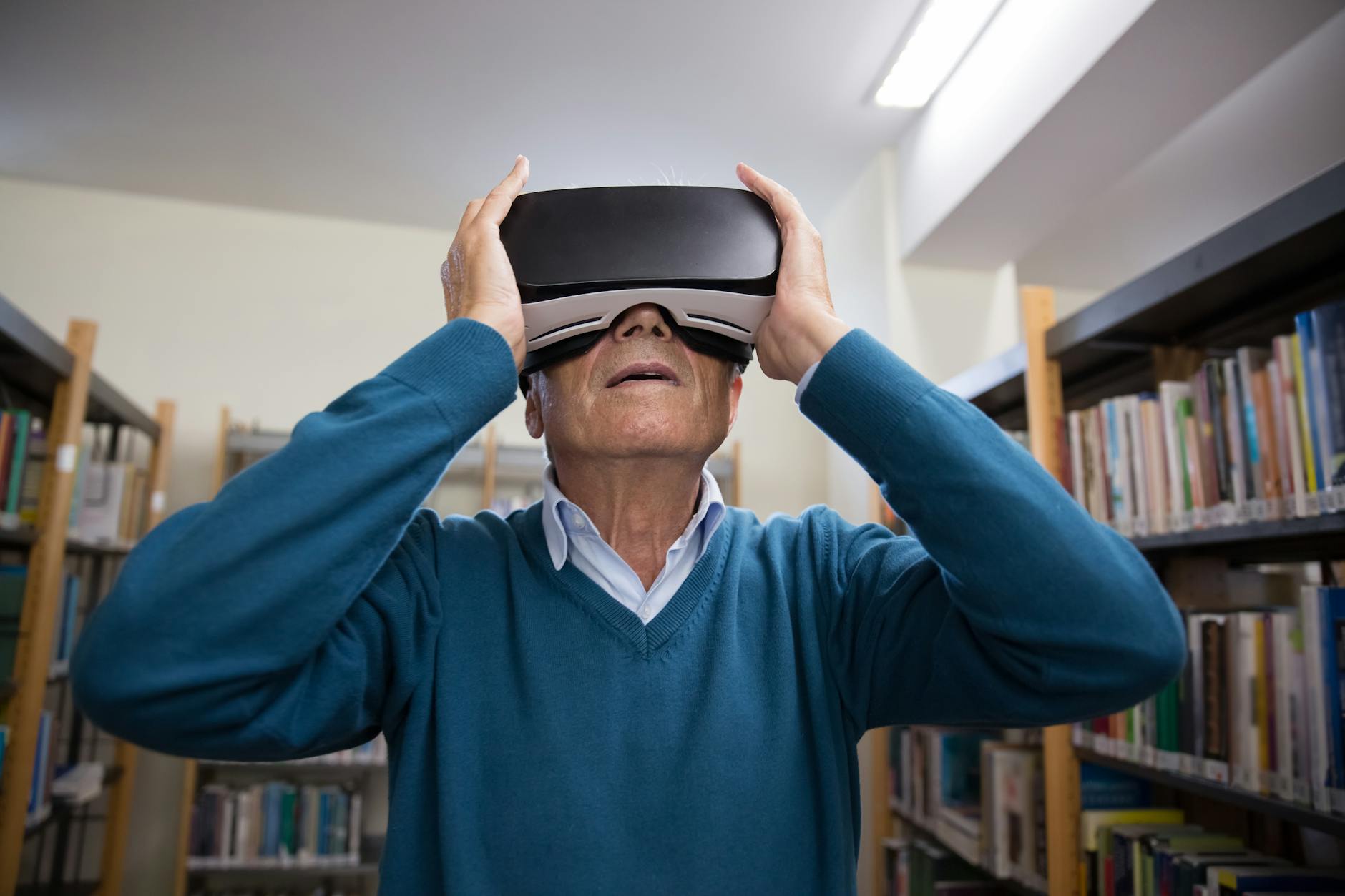 elderly man wearing vr goggles and standing in a library