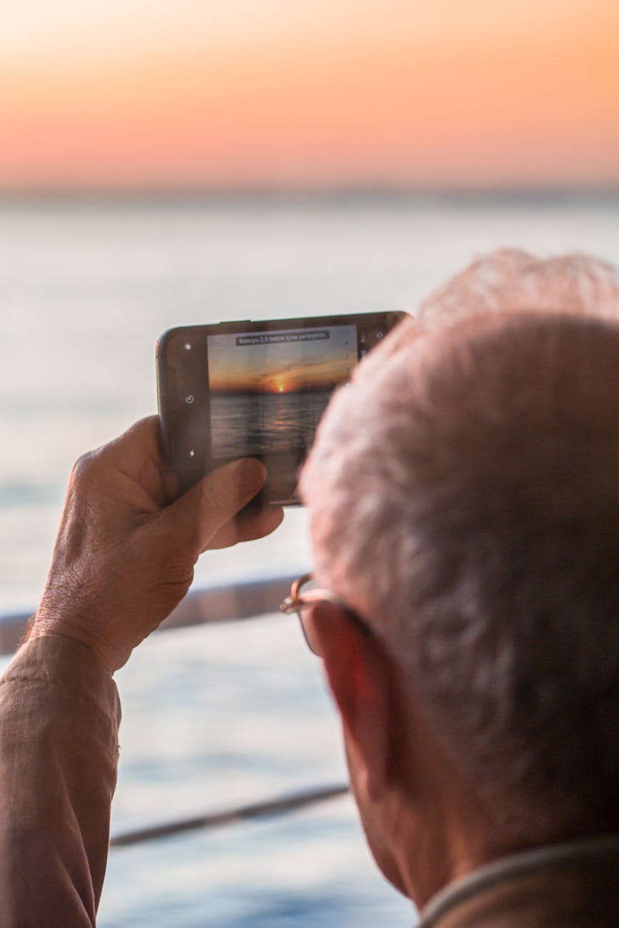 anonymous male taking photo of ocean on smartphone at sunset
